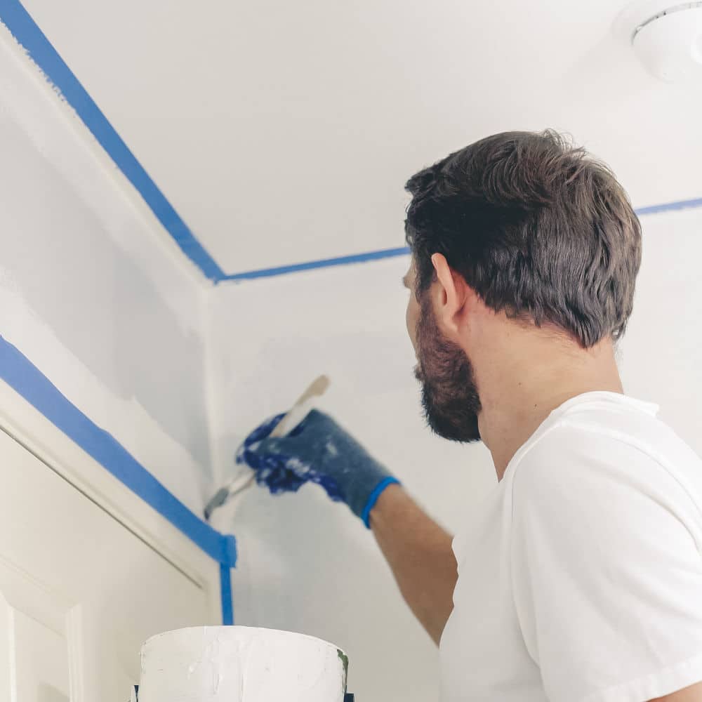 Close up of painter hands with gloves painting the wall edge by